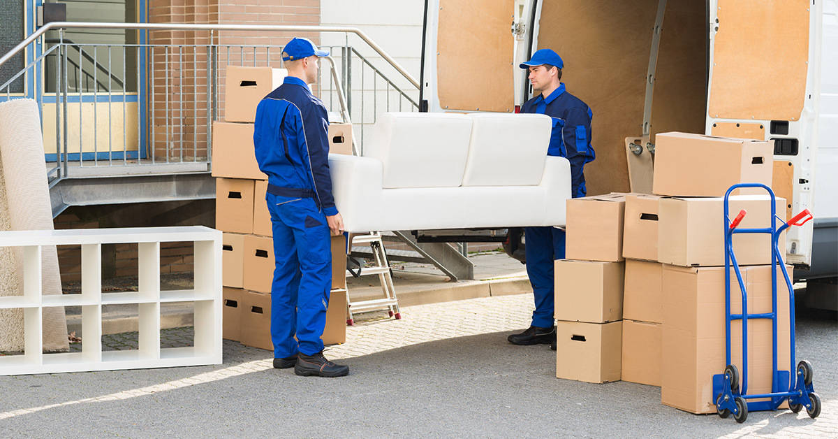 Two long-distance movers about to load a sofa onto a van.